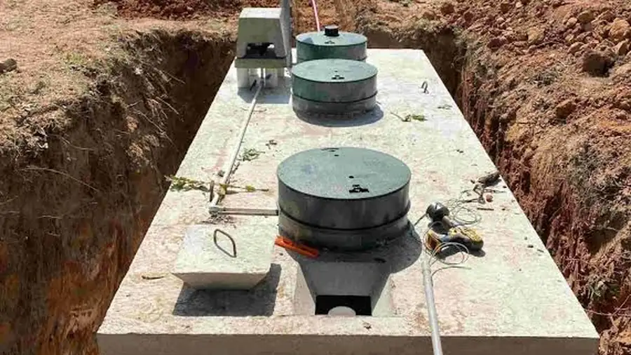 A concrete septic tank set into an excavated trench in red clay soil with three access lids visible