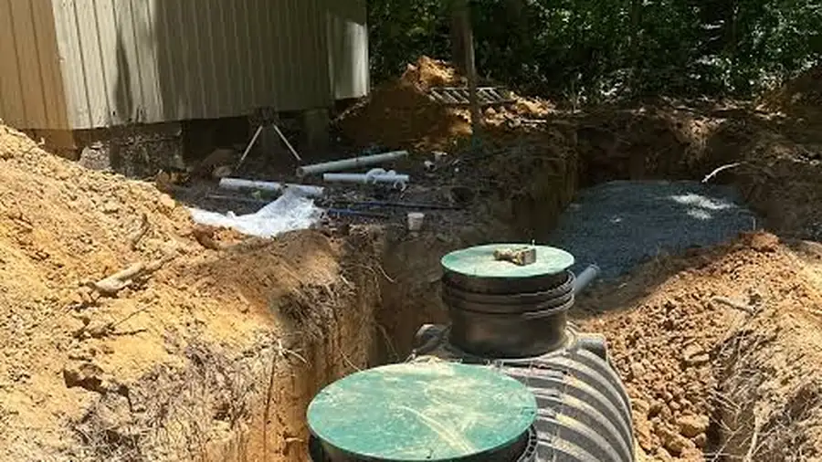Two plastic septic tanks set in an open excavated trench in clay soil beside a house
